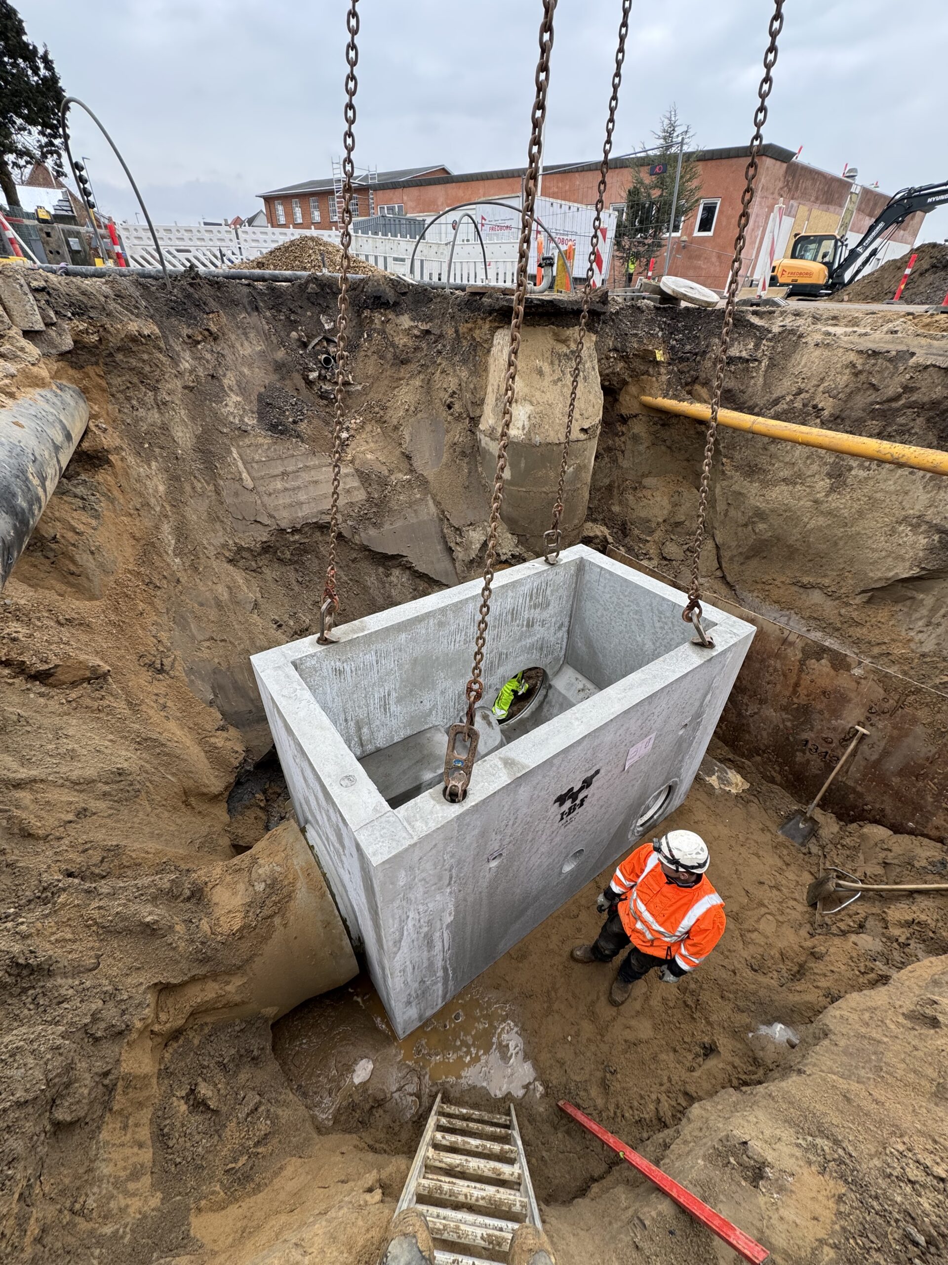 Stort betonbygværk sænkes ned i udgravningen ved kloakarbejde